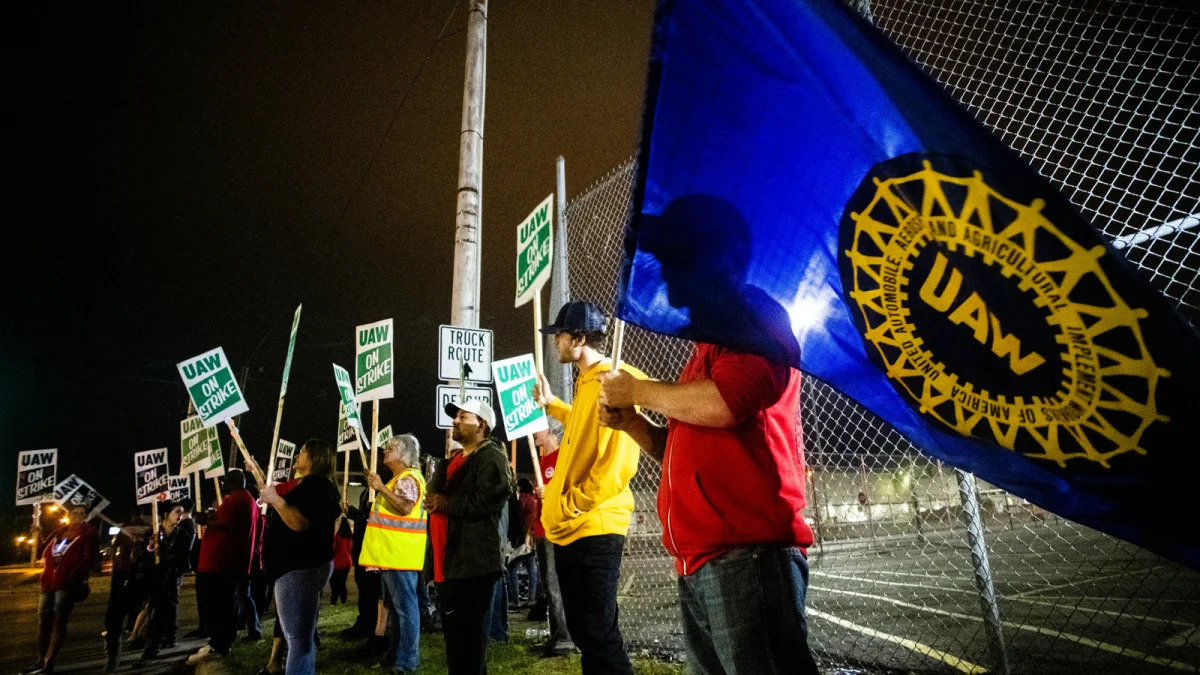 Davison resident Jeff Elkins, 37 years old, and a General Motors employee who works on the line, waves a United Auto Workers flag as employees leave the Flint Assembly Plant at midnight as part of the national strike on Monday, Sept. 16, 2019, in Flint, Michigan. More than 49,000 members of the United Auto Workers walked off General Motors factory floors or set up picket lines early Monday as contract talks with the company deteriorated into a strike. (Jake May/The Flint Journal via AP)