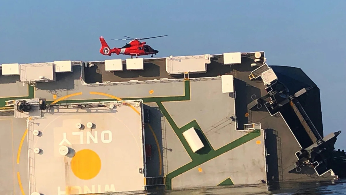 In this image released by the U.S. Coast Guard, a USCG helicopter hovers over an overturned cargo ship in St. Simons Sound, Ga., Monday, Sept. 9, 2019. The U.S. Coast Guard says rescuers have heard noises from inside the ship where multiple crew members are missing after their huge vessel overturned and caught fire off Georgia's coast.   (U.S. Coast Guard via AP)