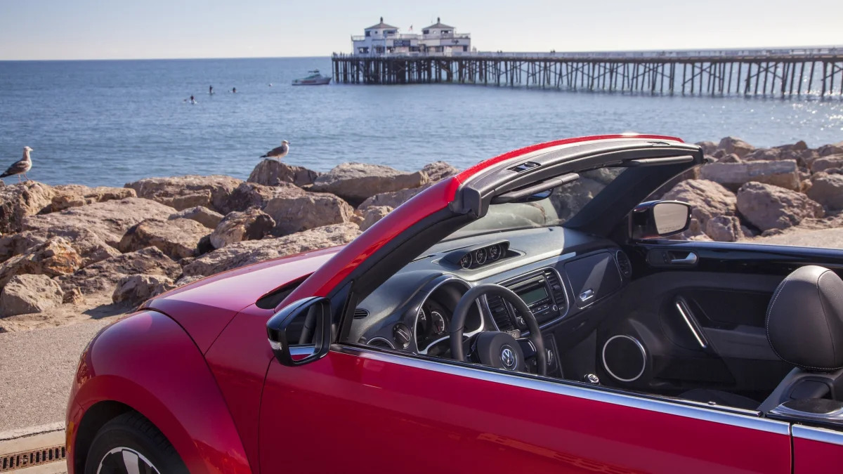 VW Beetle convertible in red by a pier at the ocean