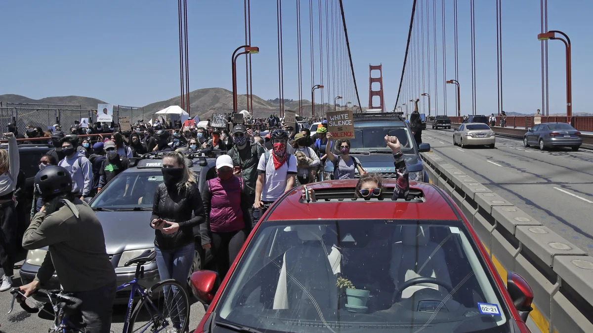 A motorist raises her fist through the sunroof of her car while marchers walk past as traffic is stopped on the Golden Gate Bridge in San Francisco, Saturday, June 6, 2020, at a protest over the Memorial Day death of George Floyd. Floyd died May 25 after being restrained by Minneapolis police. (AP Photo/Jeff Chiu)