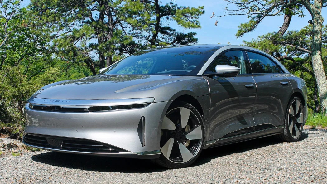 A silver Lucid Air Grand Touring Performance electric car in a driveway, with trees and blue sky in the background.