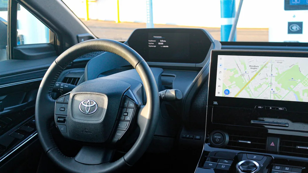 The steering wheel and screens in the 2023 Toyota bZ4X AWD Limited electric SUV, viewed from the back seat.