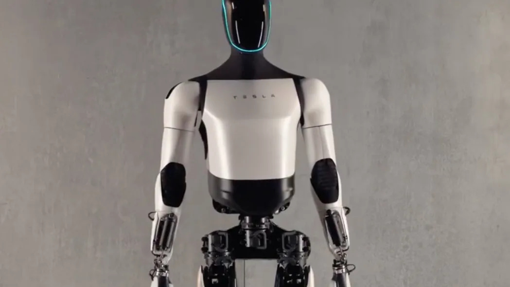 Photo of Tesla's humanoid robot called Optimus. It has white body parts and an all-black head with a blue light