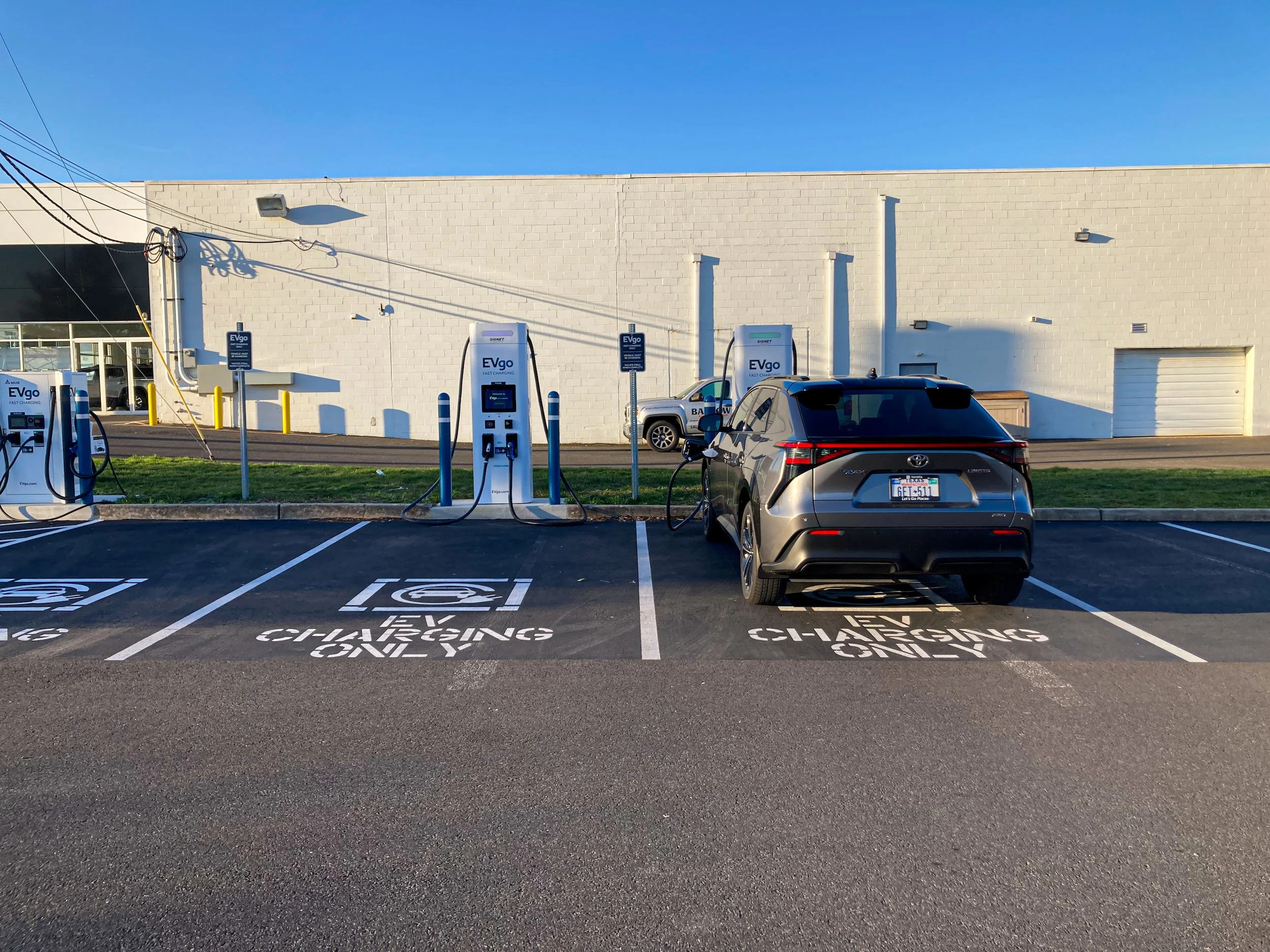 The 2023 Toyota bZ4X AWD Limited electric SUV parked in a parking lot, with a white building and blue skies in the background.