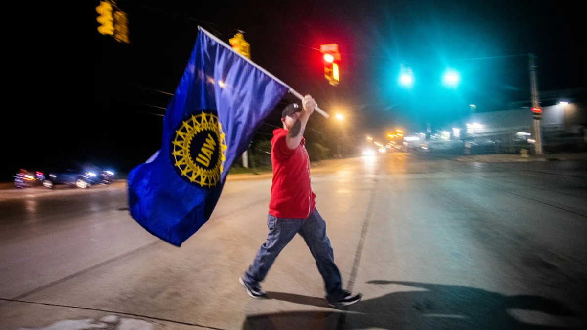 Davison resident Jeff Elkins, 37 and a GM employee who works on the line, walks across Van Slyke Road proudly waving a UAW flag as General Motors employees leave the Flint Assembly Plant at midnight as part of the national strike on Monday, Sept. 16, 2019 in Flint, Michigan. (Jake May/The Flint Journal via AP)
