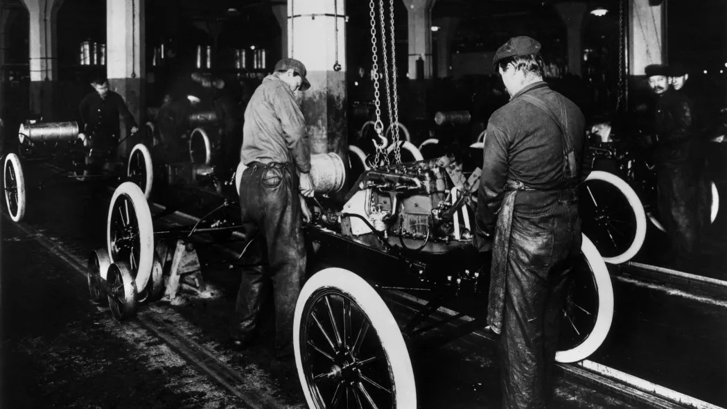 1914: Workers constructing a Model-T engine on an assembly line in a Ford Motor Company factory.