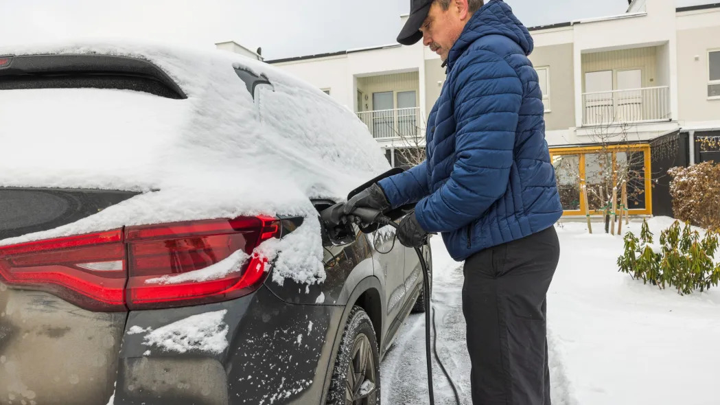 Man connecting a charging cable to an electric car charging station on a snowy winter day in Sweden.