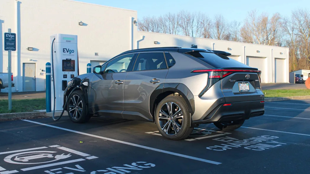 The 2023 Toyota bZ4X AWD Limited electric SUV sits in the shade, parked by a charging stall.